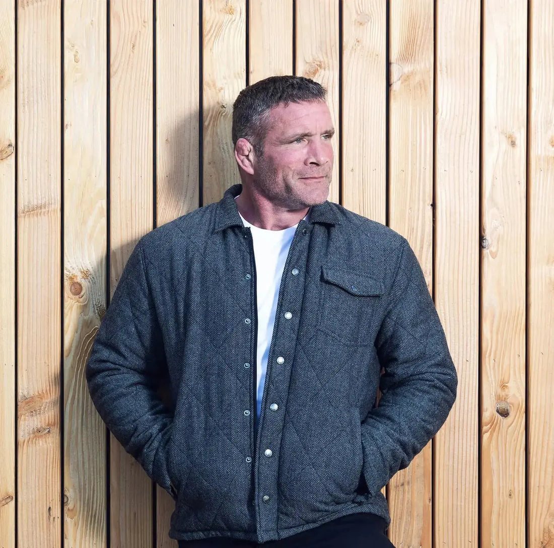 Winter Coats and Jackets Raging Bull Clothing, A man leaning against a wooden wall, wearing Raging Bull coat. 