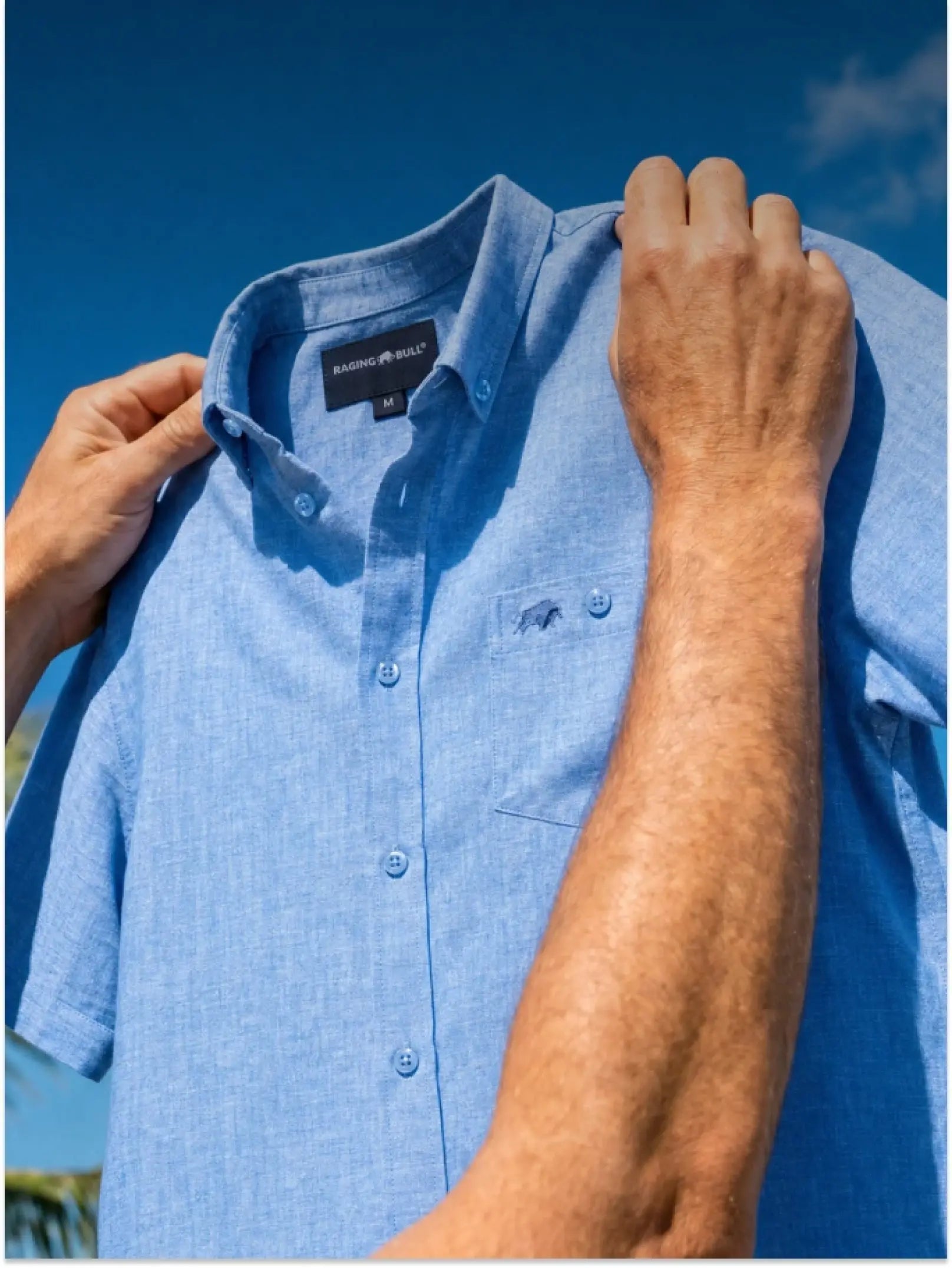 A man in a summer short sleeve shirt in blue, wearing navy shorts. 