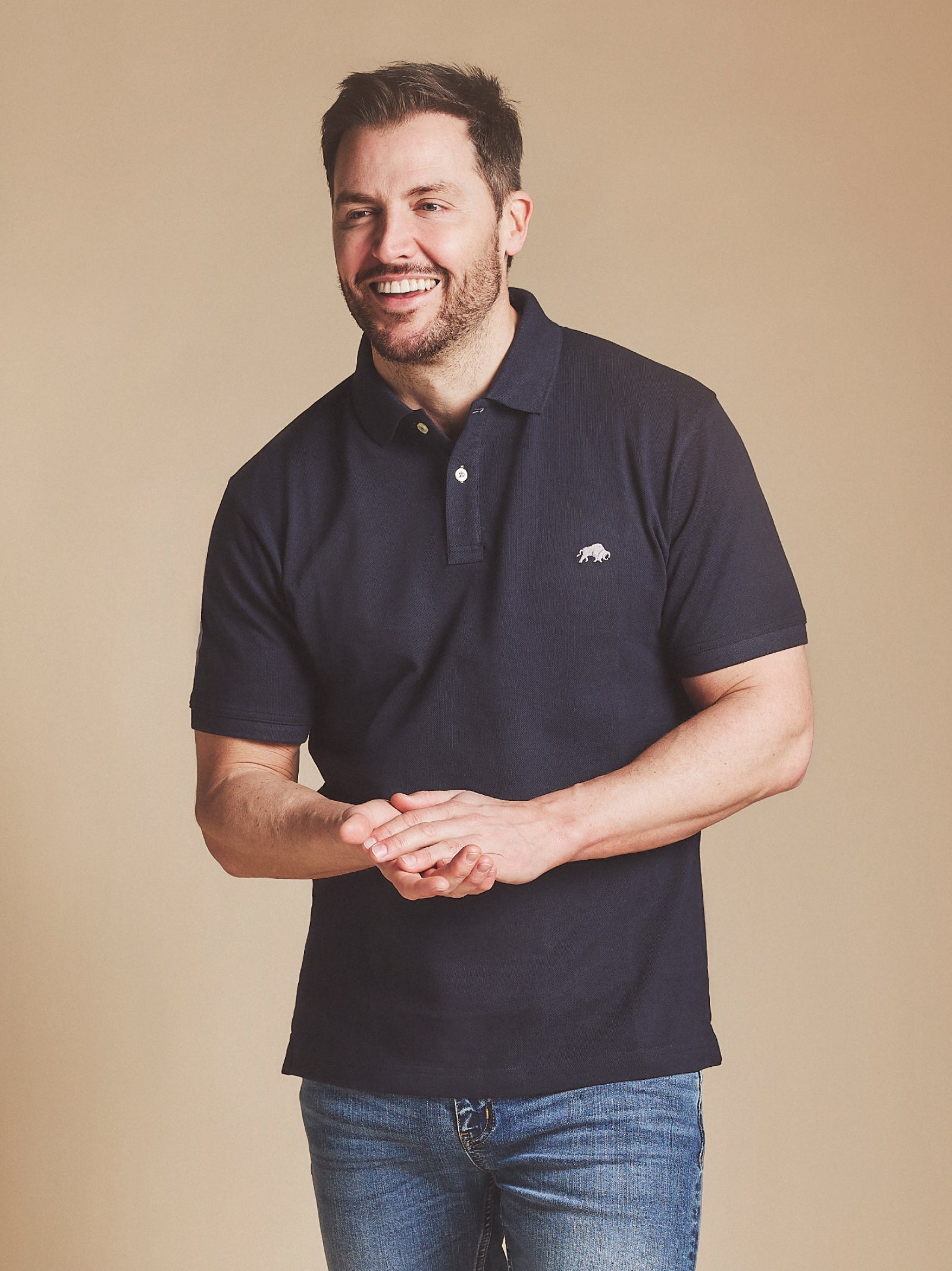 Man in a red polo shirt sitting on a stone wall outdoors, looking to the side.