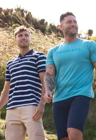 Two men in casual summer outfits walking outdoors, one in a striped polo and the other in a blue T-shirt.