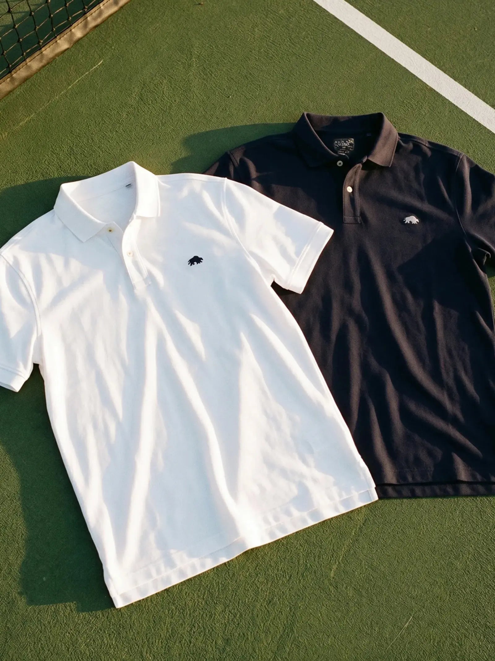 Dark Raging Bull polos and shirts draped over a tree branch in a sunlit forest.