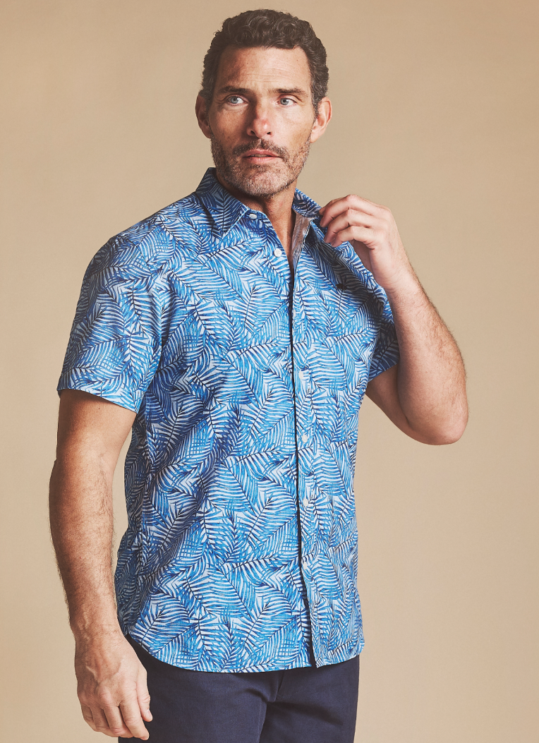 A man in a summer short sleeve shirt in blue, wearing navy shorts. 