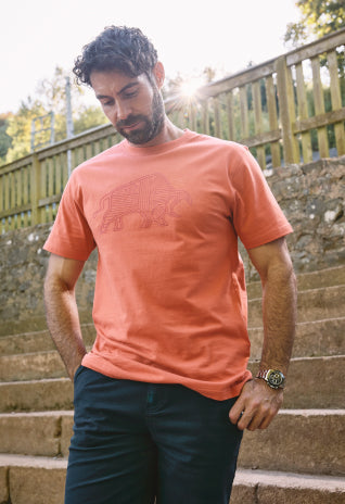 Man in an orange graphic T-shirt and dark trousers standing on outdoor steps, looking down.