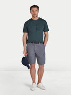 Man wearing a green t-shirt and gray shorts holding a cap on a white background
