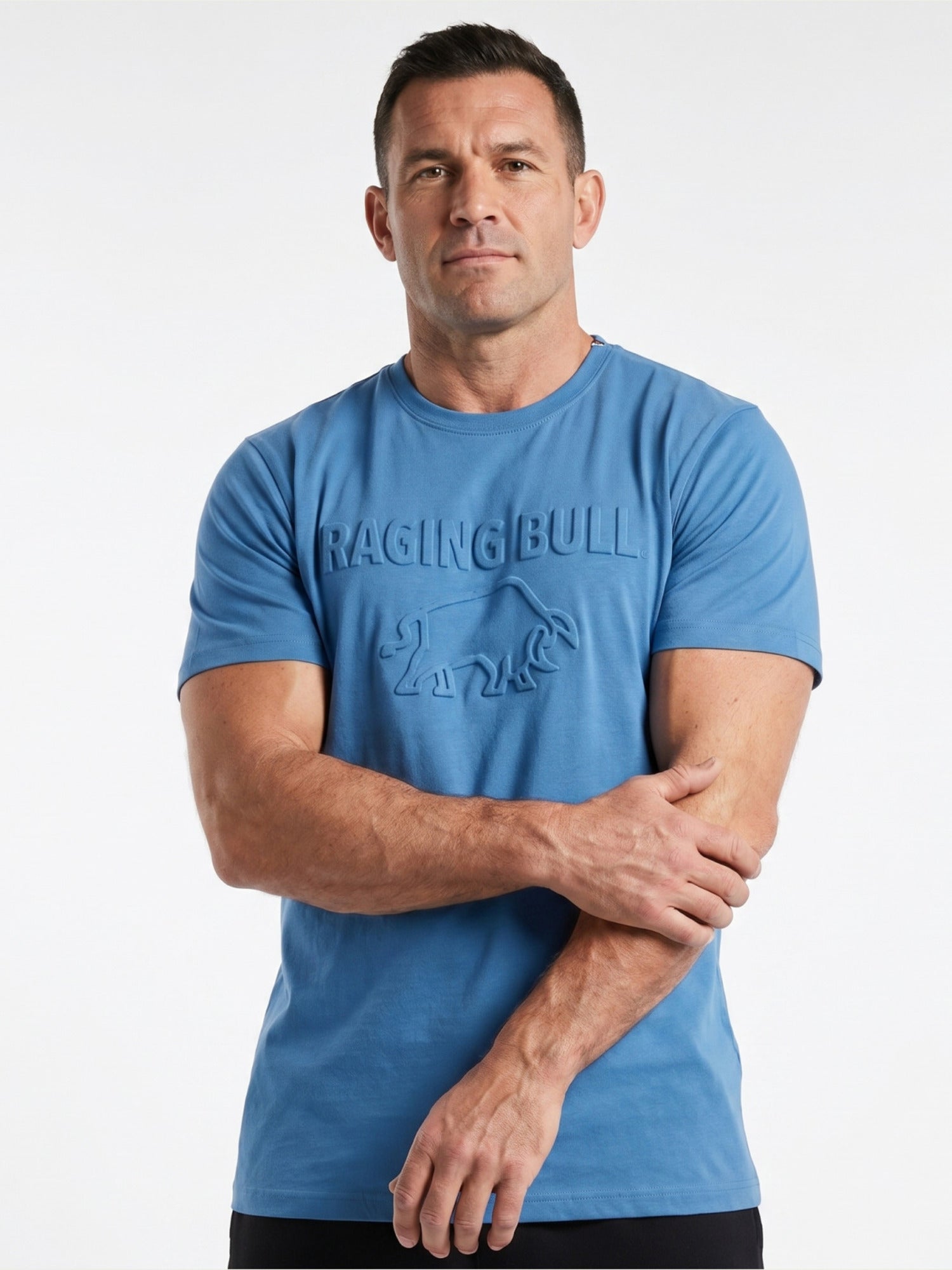 Man wearing a blue 'Raging Bull' t-shirt with arms crossed on a white background
