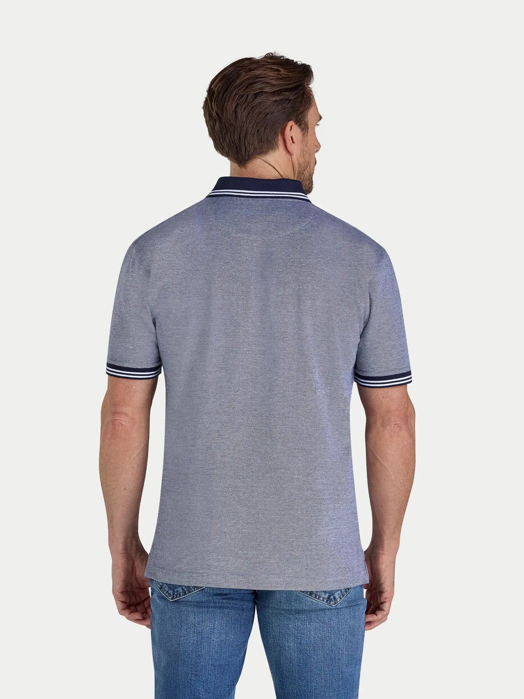 Man wearing a navy polo shirt with blue jeans on a white background
