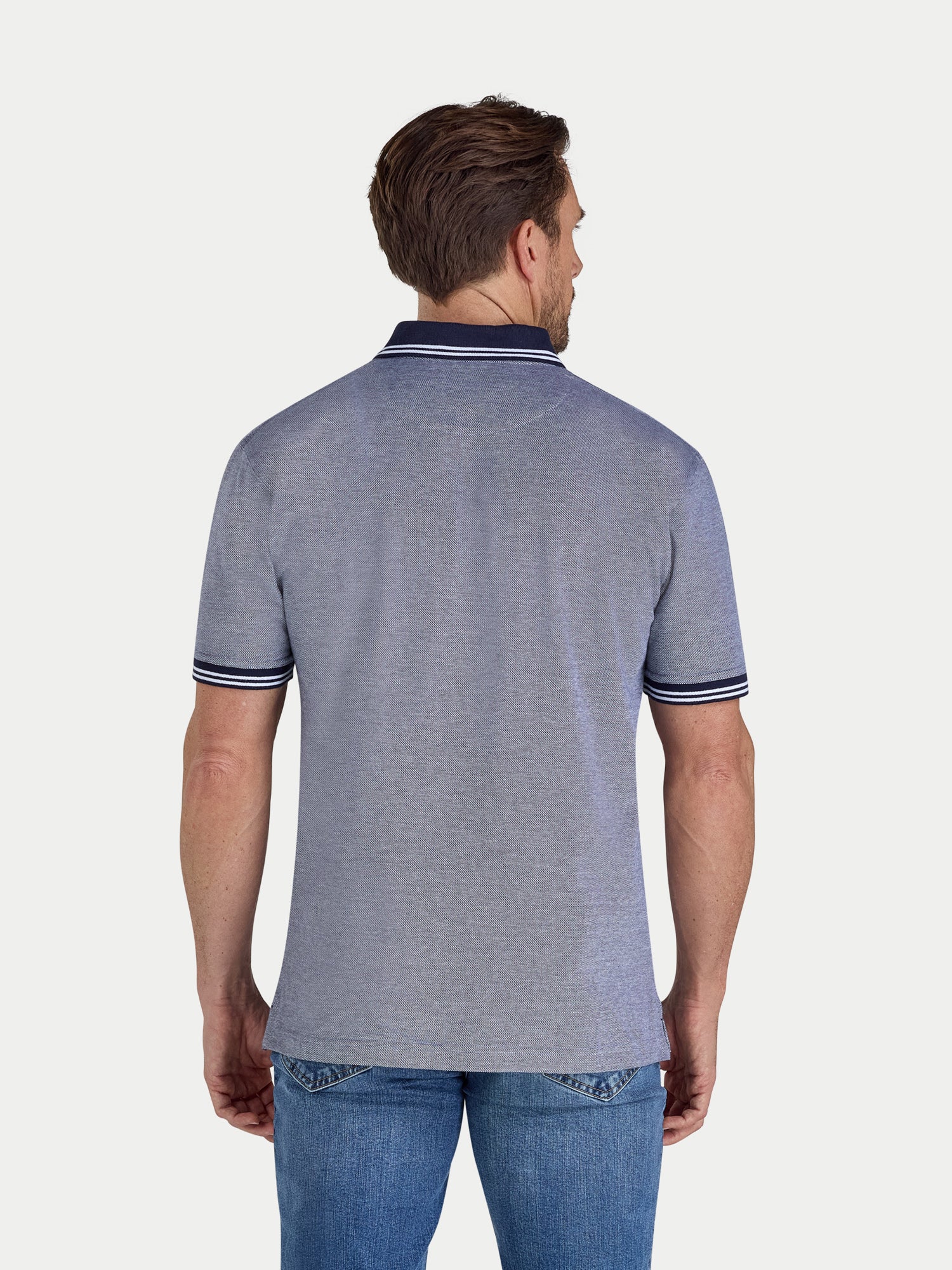 Man wearing a navy polo shirt with blue jeans on a white background