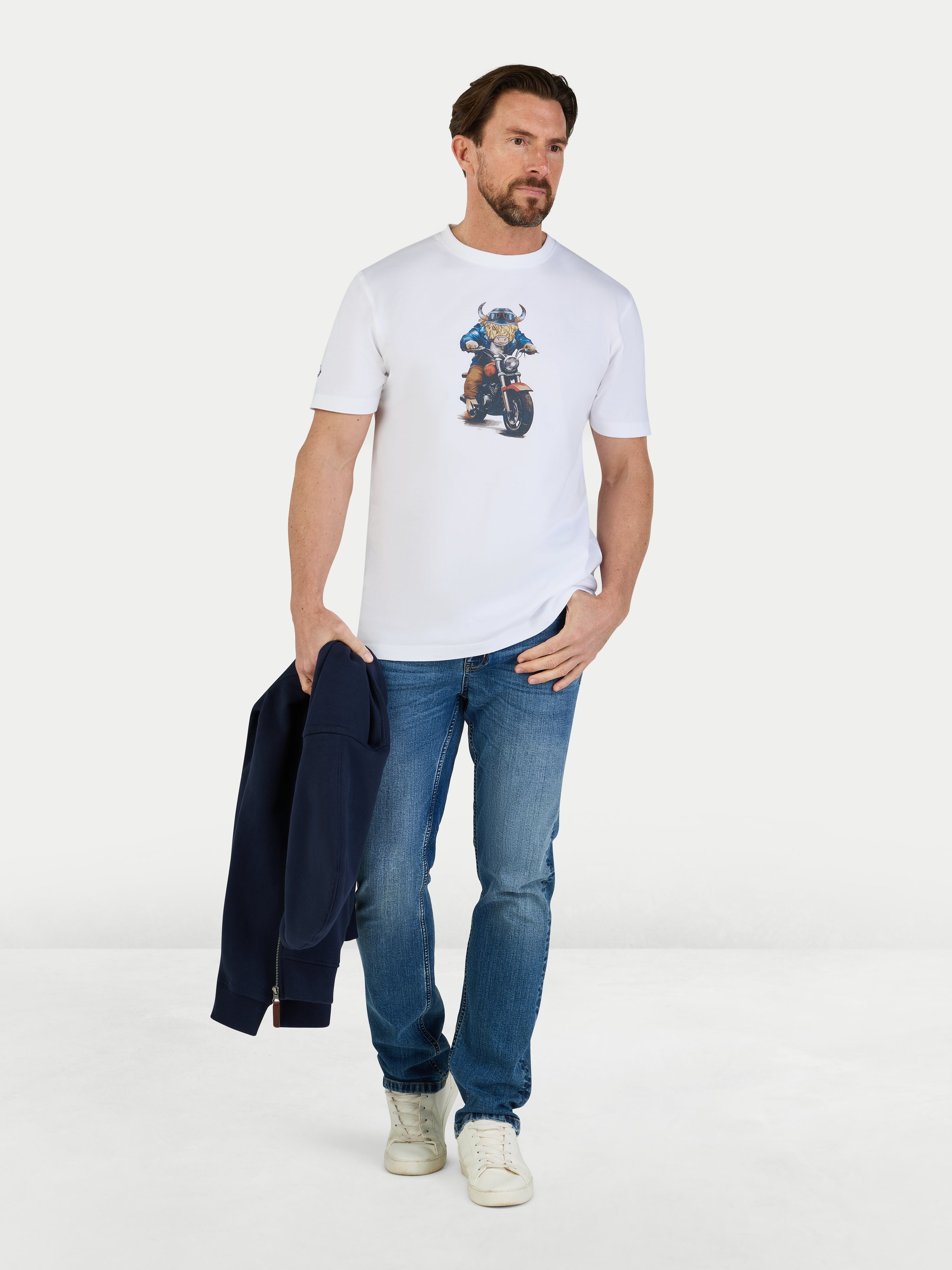 Man wearing a white t-shirt with a graphic design and blue jeans, holding a dark jacket.