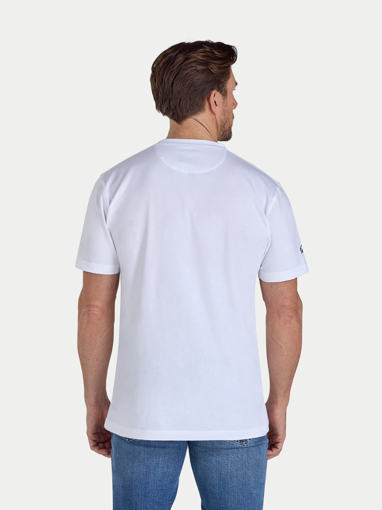 Man wearing a plain white t-shirt and blue jeans on a light gray background