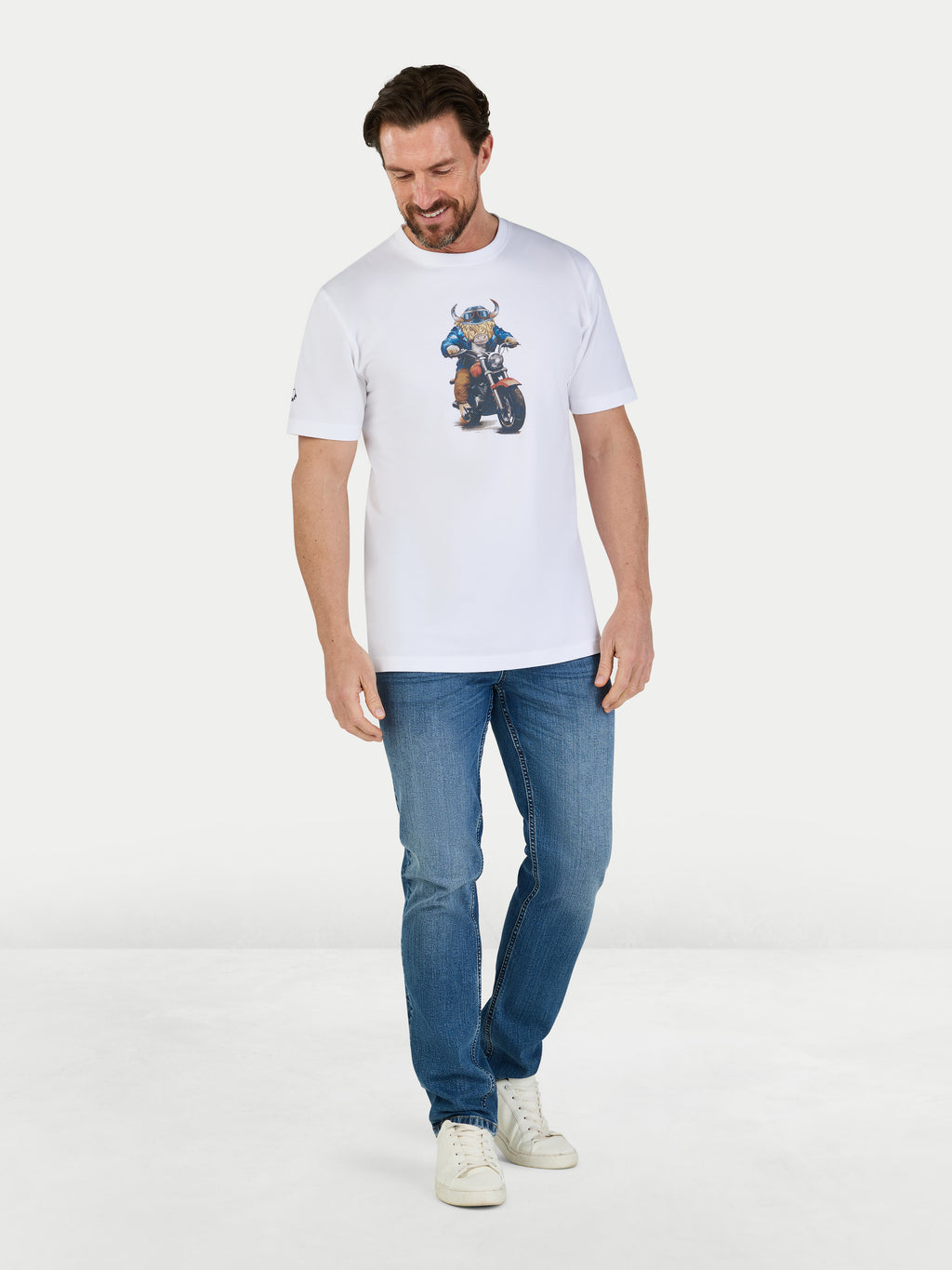 Man wearing a white t-shirt with a graphic design and blue jeans on a light gray background