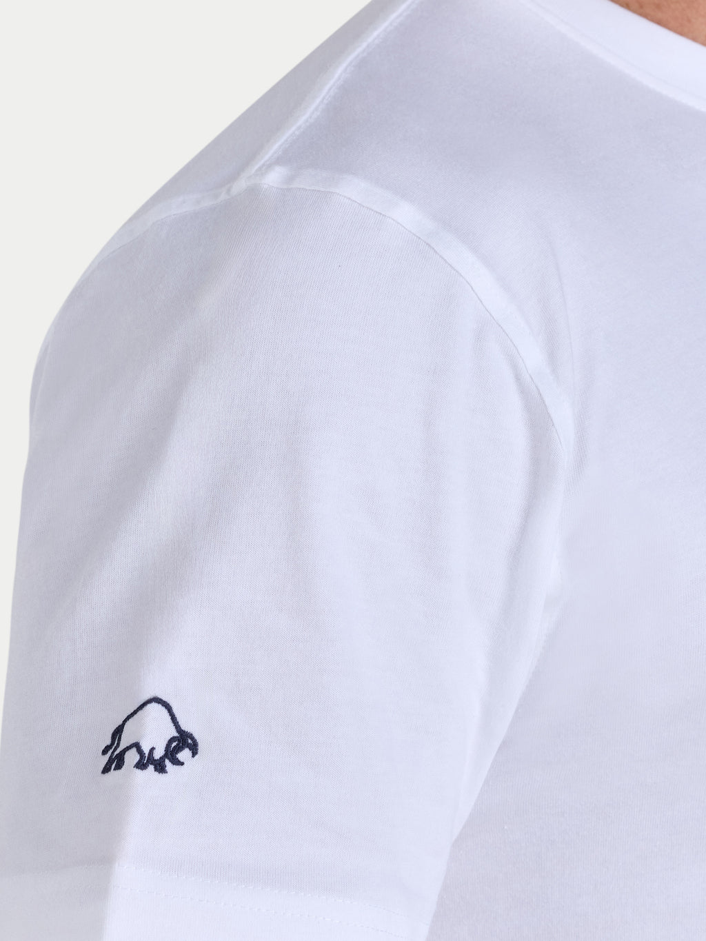 White t-shirt with a small black logo on the sleeve against a light gray background