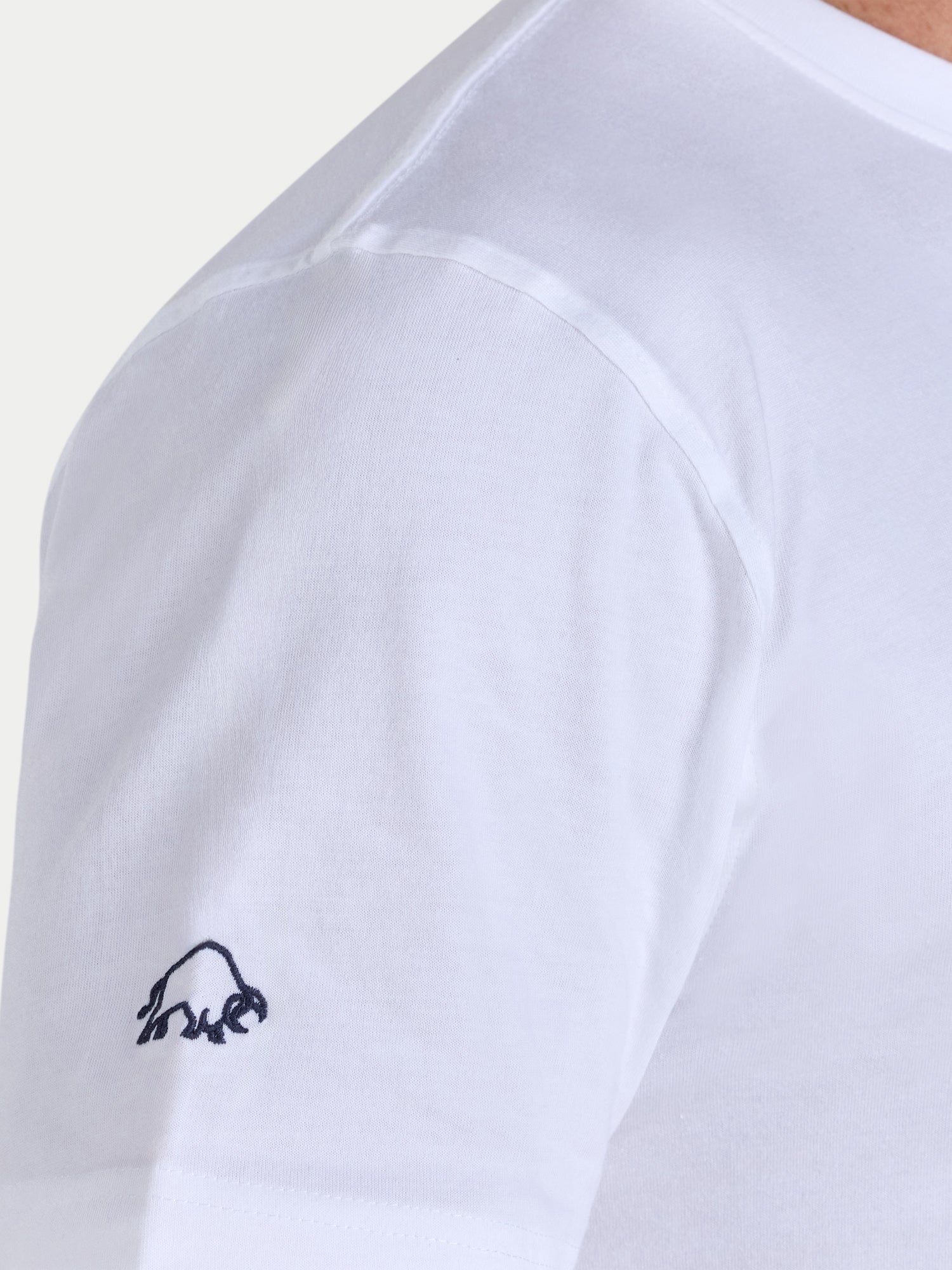 White t-shirt with a small black logo on the sleeve against a light gray background
