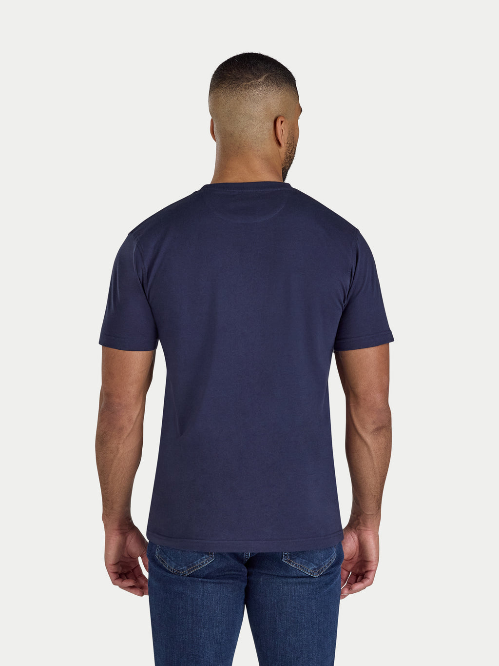 Man wearing a navy blue t-shirt and jeans on a white background