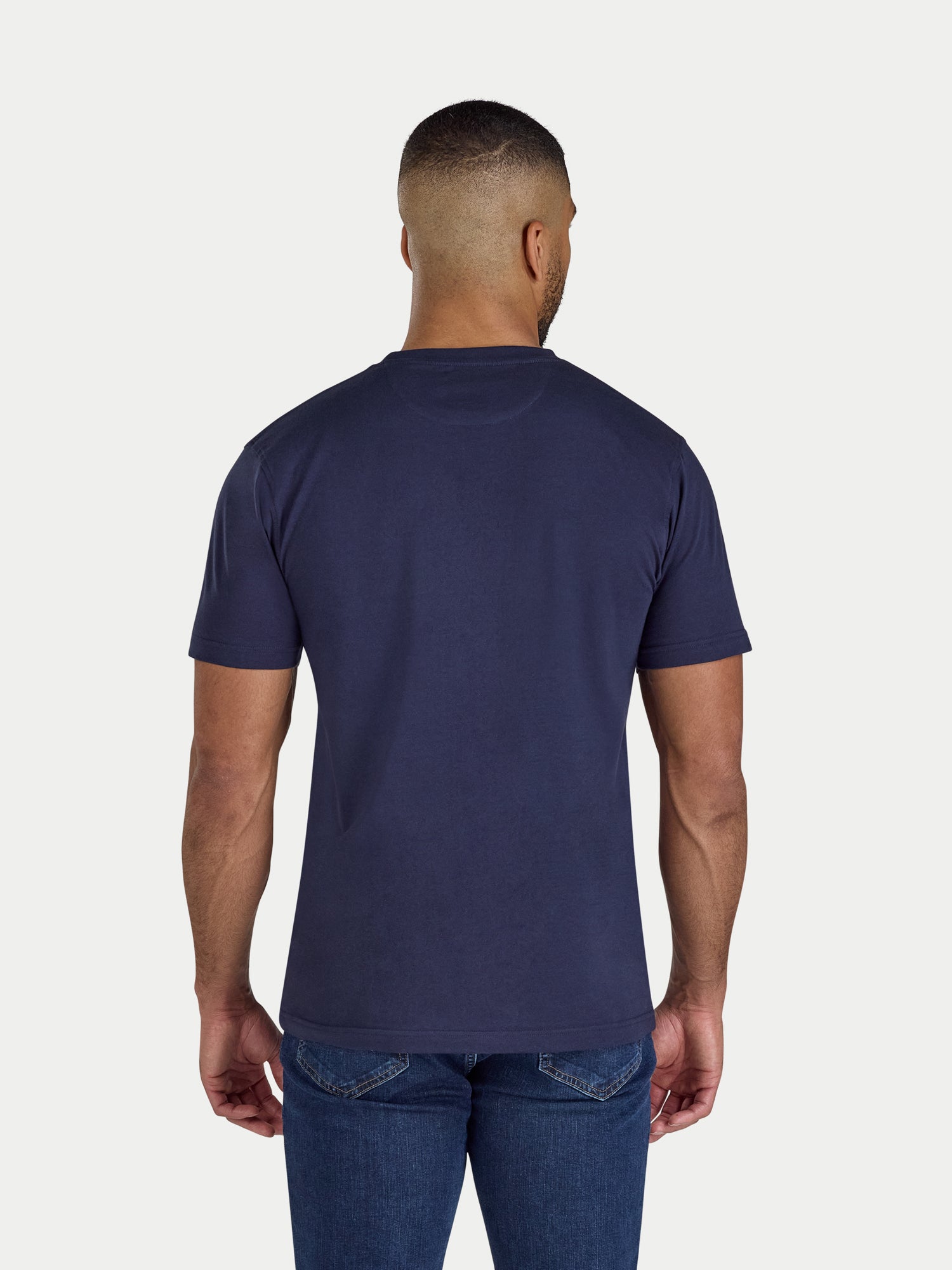 Man wearing a navy blue t-shirt and jeans on a white background