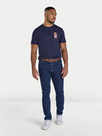 Man wearing a navy t-shirt with a logo and blue jeans on a white background