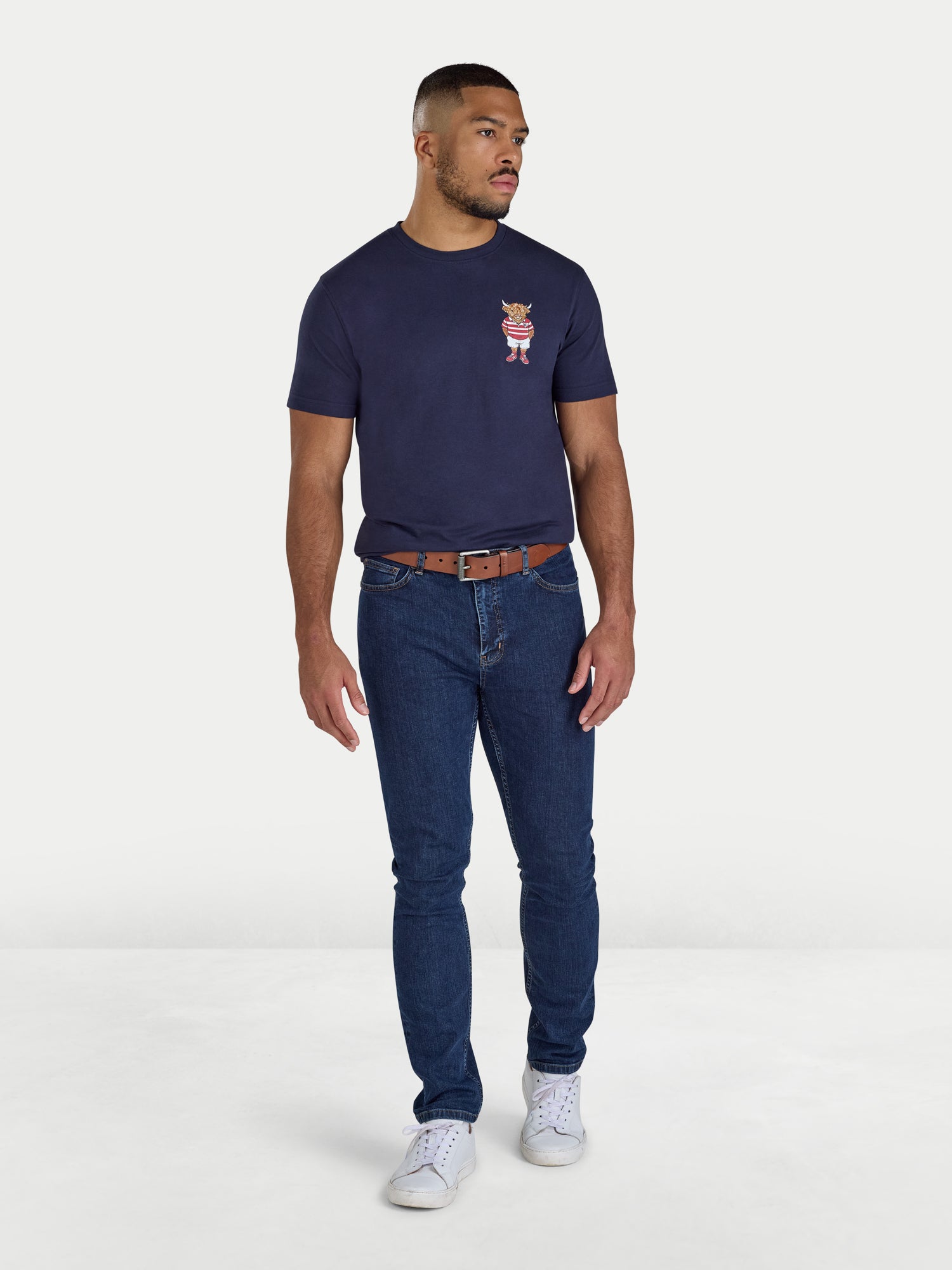 Man wearing a navy t-shirt with a logo and blue jeans on a white background