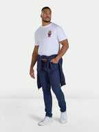 Man wearing a white t-shirt with a graphic design, blue jeans, and white sneakers on a white background