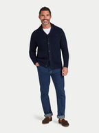 Man wearing a navy cardigan, white shirt, blue jeans, and brown shoes on a light gray background