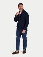 Man wearing a navy cardigan, blue jeans, and brown shoes on a white background
