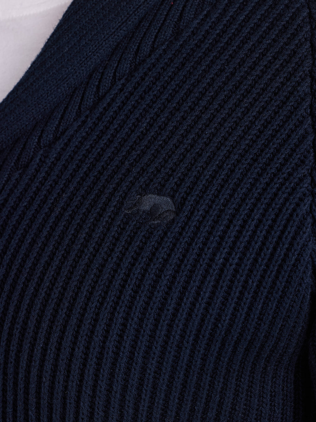 Close-up of a dark blue ribbed sweater with a brand logo.