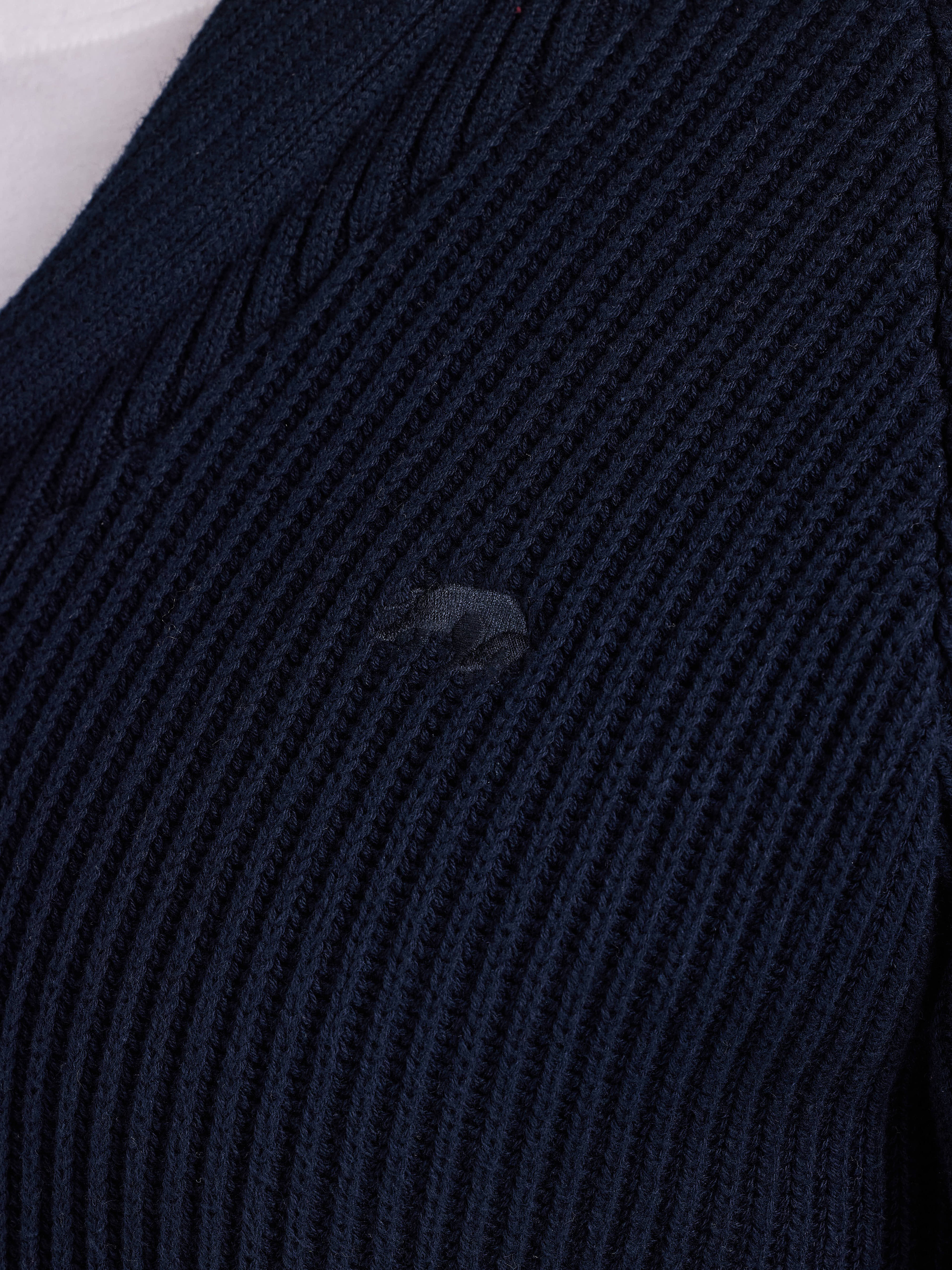 Close-up of a dark blue ribbed sweater with a brand logo.