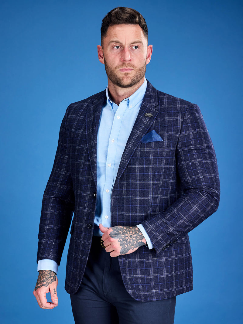 A man wearing a navy blue checkered wool blazer with a patterned pocket square, a chest pocket, and a metal bull logo on the lapel.