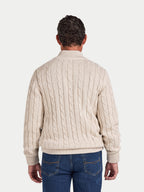 Man wearing a cream cable knit sweater and blue jeans on a white background