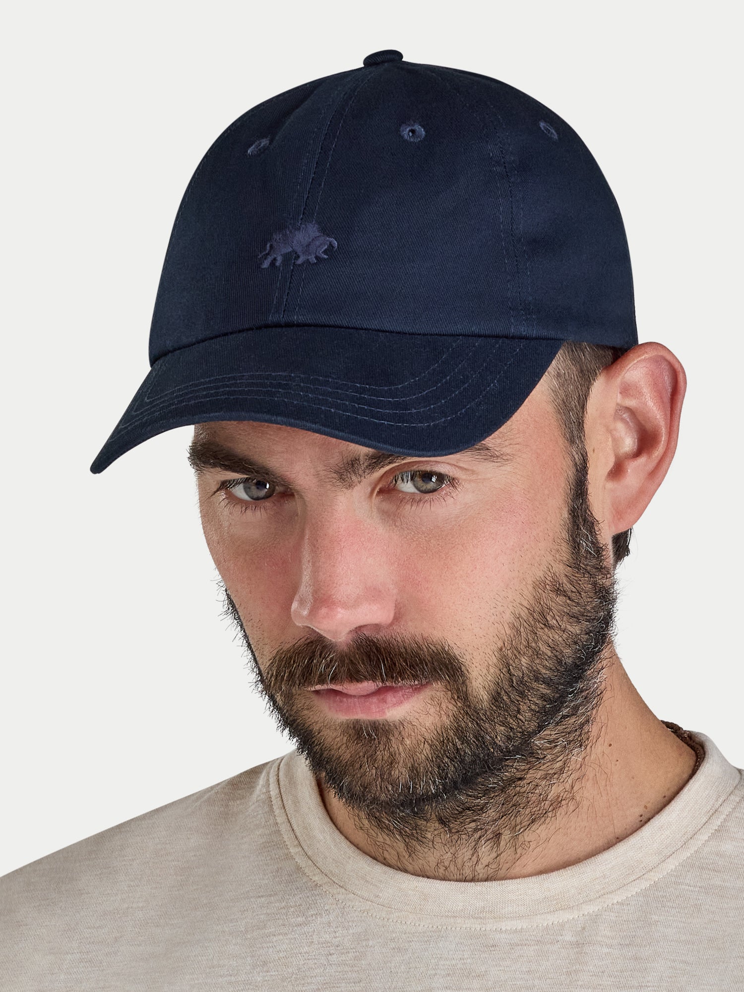 Man wearing a navy blue cap with a logo on a white background