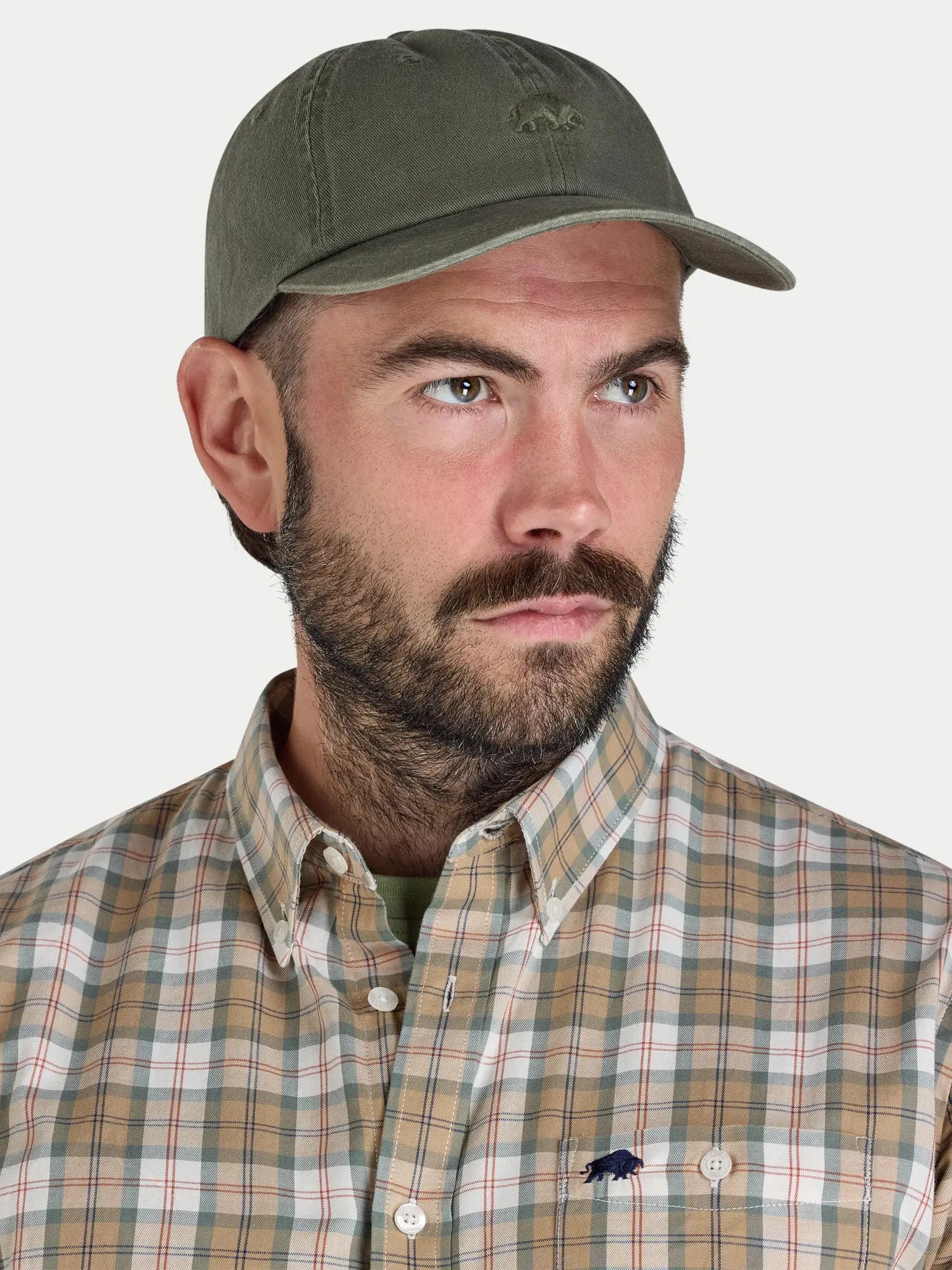 Man wearing a green cap and plaid shirt with a logo on a light gray background