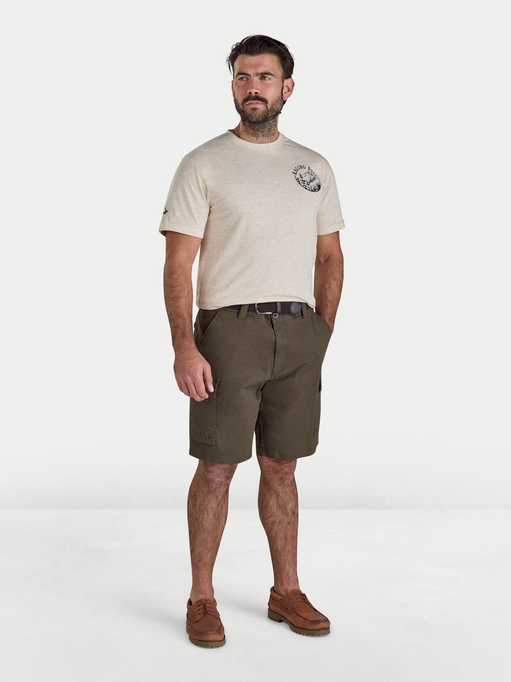 Man wearing a beige t-shirt with a logo and green shorts on a white background