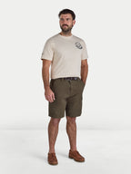 Man wearing a beige t-shirt with a logo and green shorts on a white background