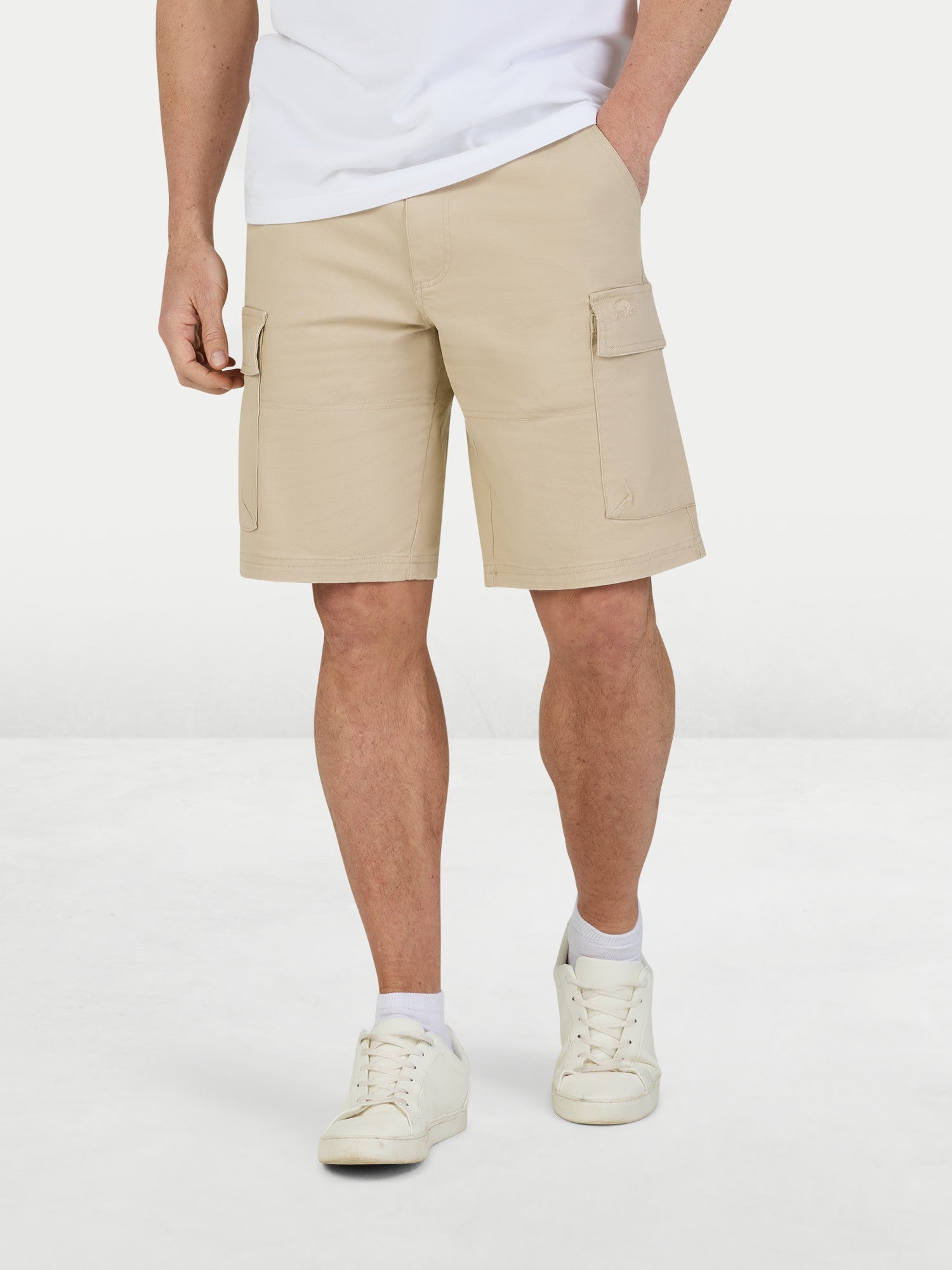 Man wearing a white t-shirt and beige shorts on a light gray background