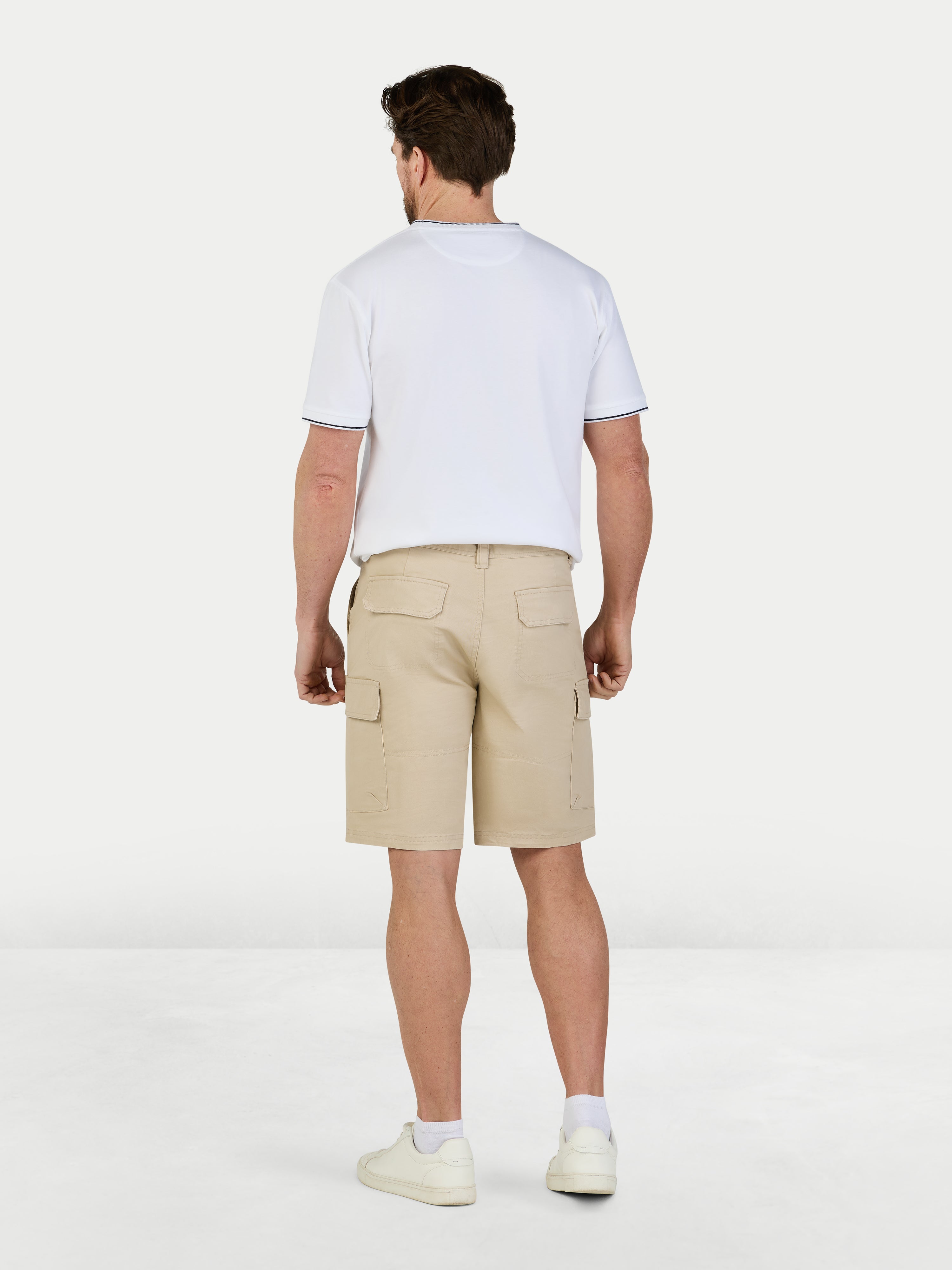 Man wearing beige cargo shorts and a white t-shirt on a white background
