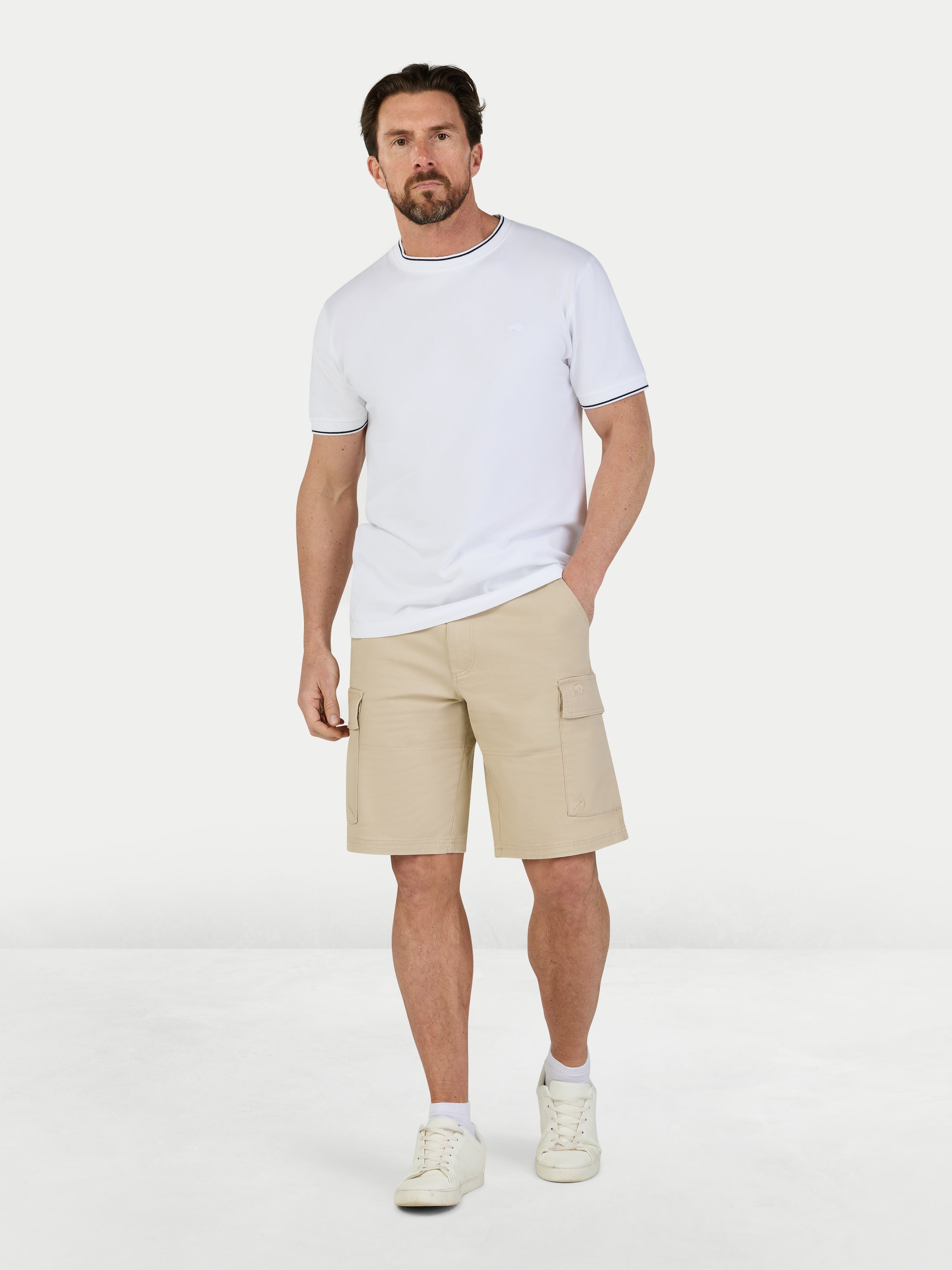 Man wearing a white t-shirt and beige shorts on a light gray background