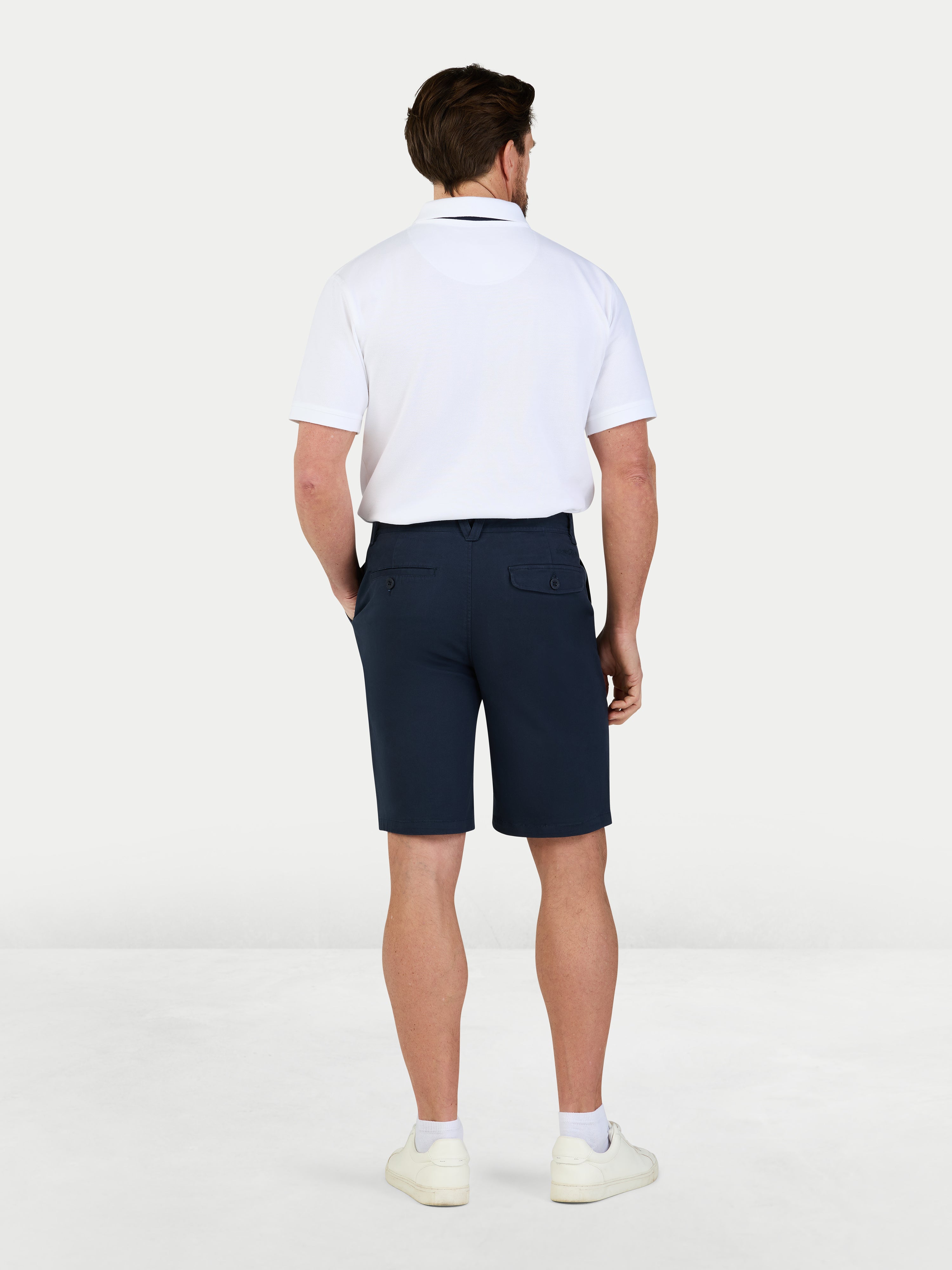 Man wearing a white polo shirt and navy shorts on a white background