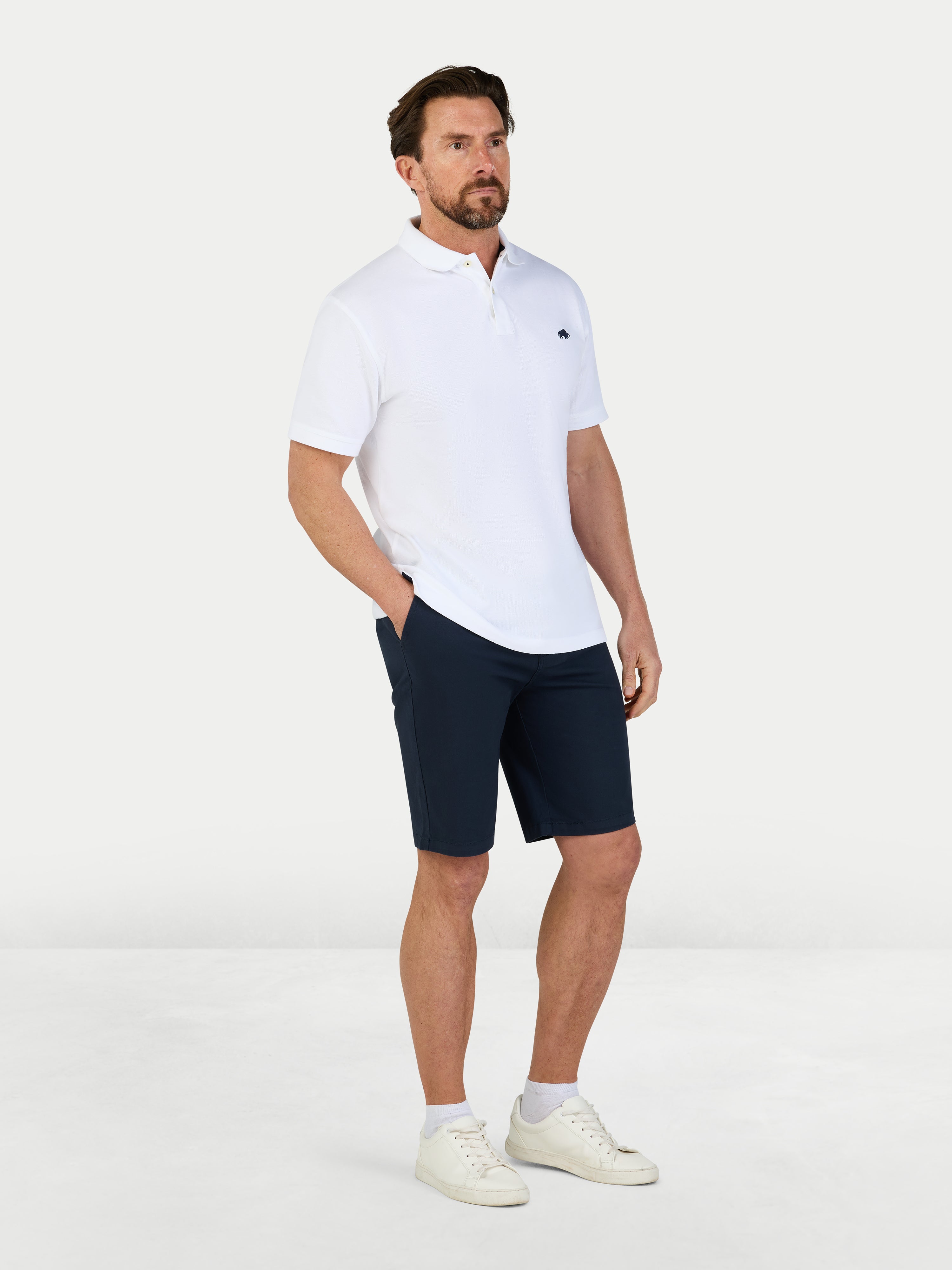 Man wearing a white polo shirt and navy shorts on a white background