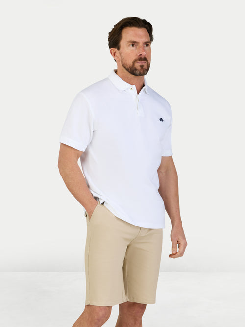 Man wearing a white polo shirt and beige shorts on a light gray background