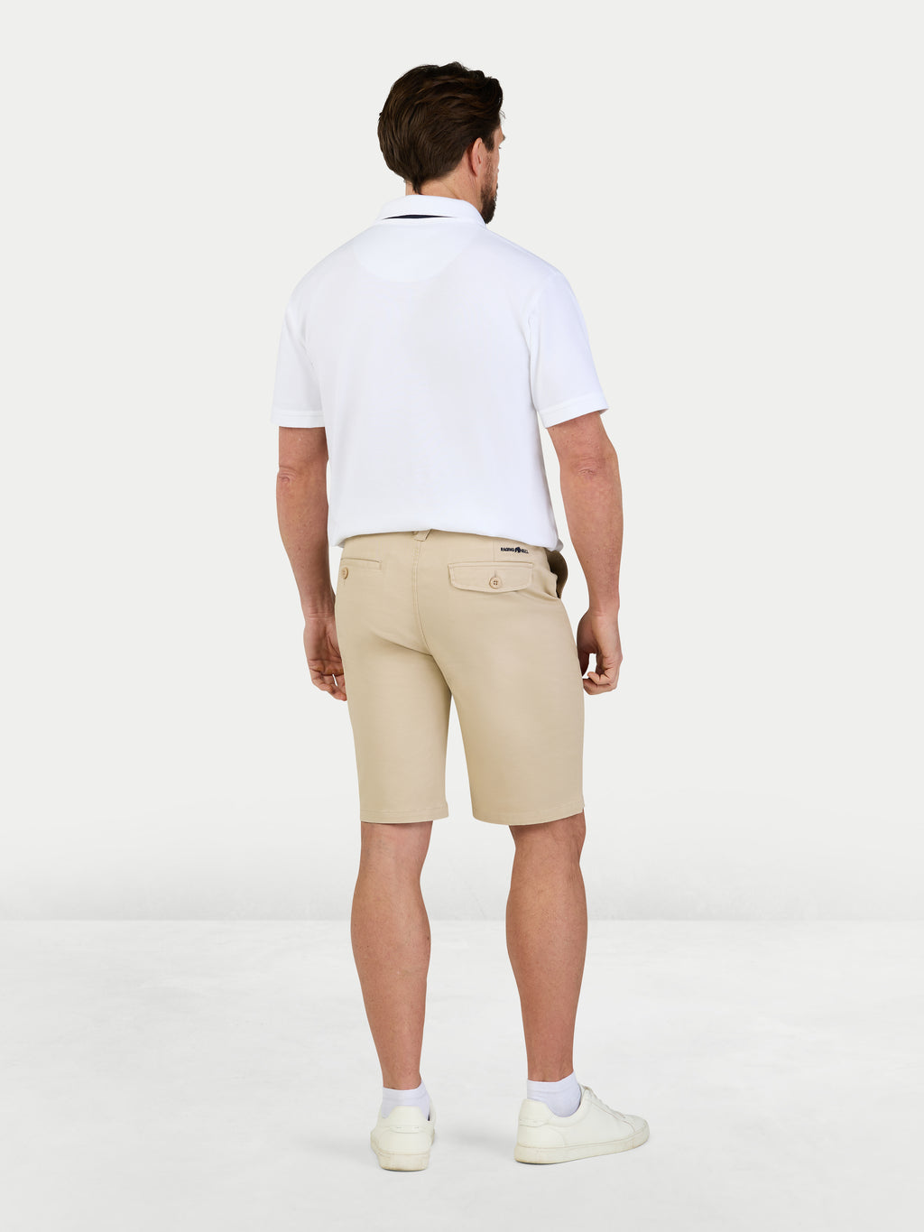 Man wearing a white polo shirt and beige shorts on a white background