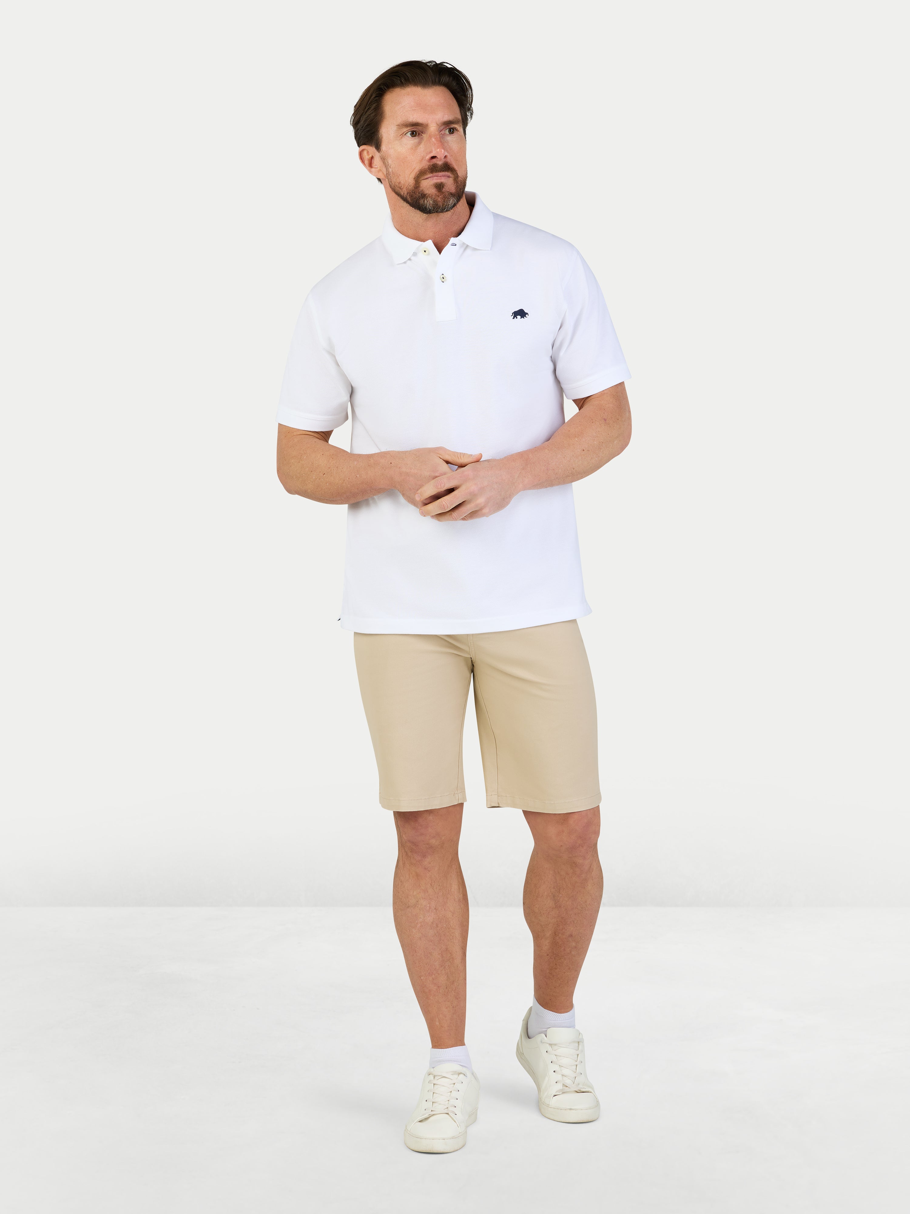 Man wearing a white polo shirt and beige shorts on a white background
