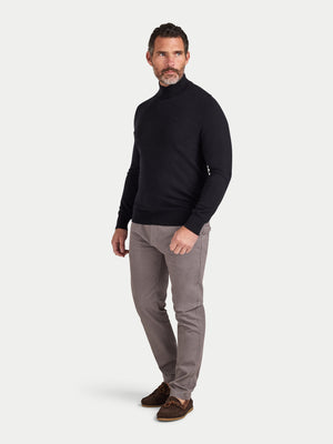Man wearing a black turtleneck and gray pants on a white background