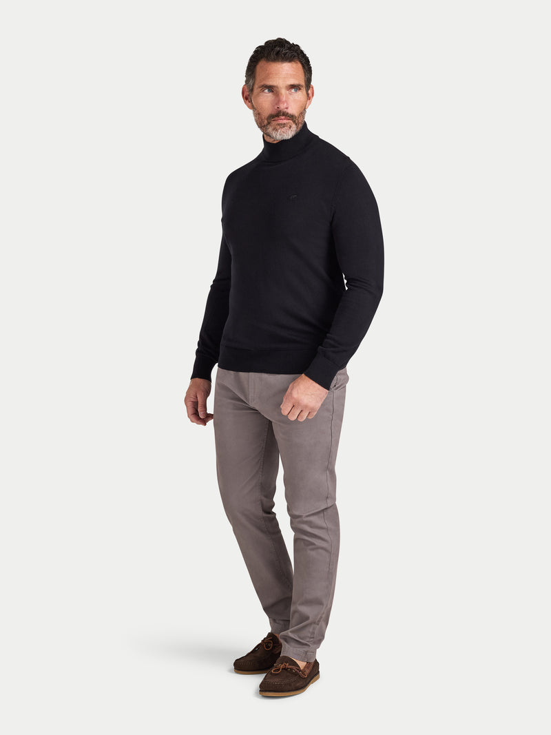 Man wearing a black turtleneck and gray pants on a white background