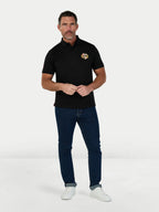 Man wearing a black polo shirt with a logo and blue jeans on a white background