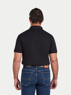 Man wearing a black polo shirt and blue jeans on a white background