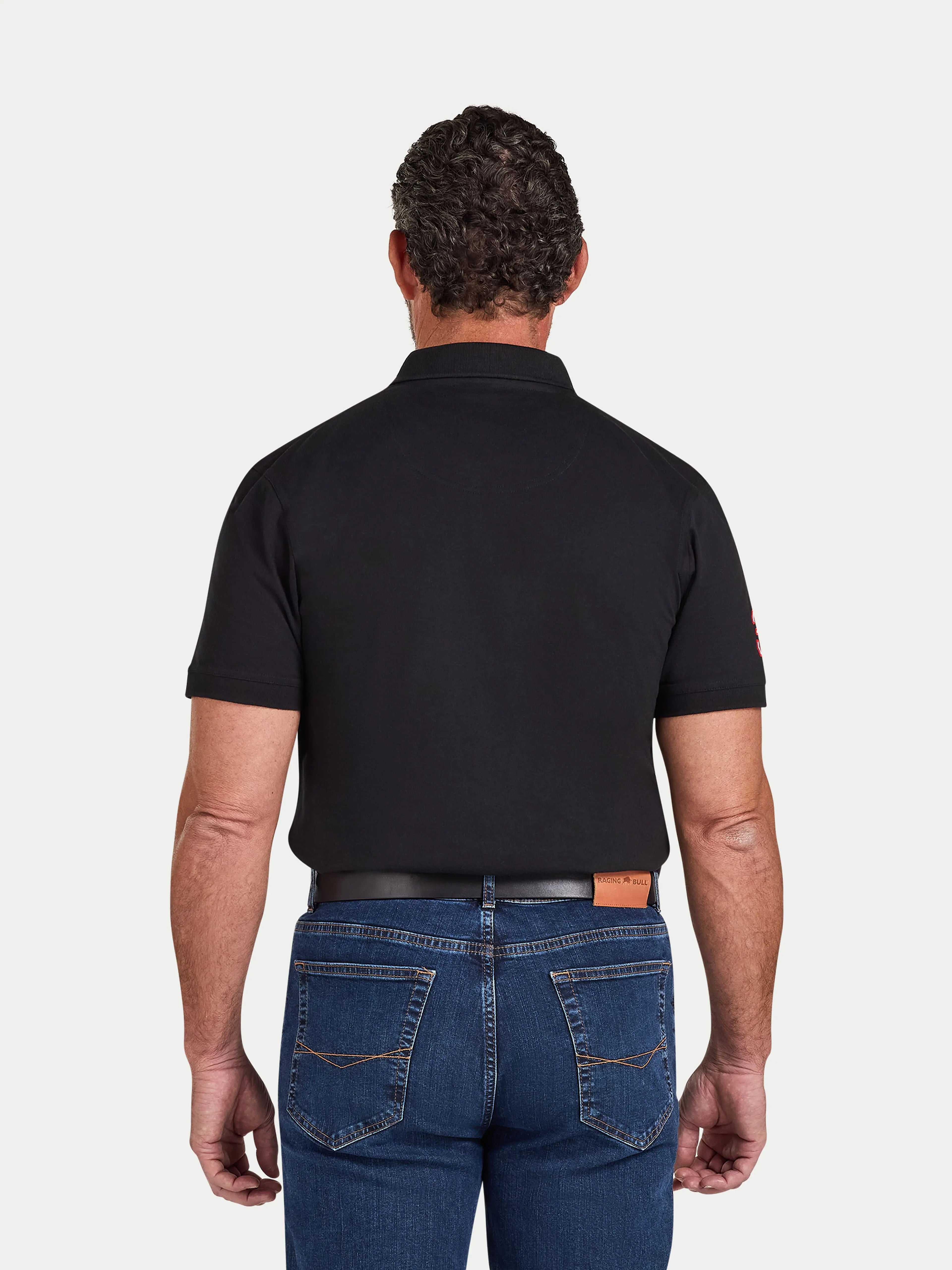 Man wearing a black polo shirt and blue jeans on a white background