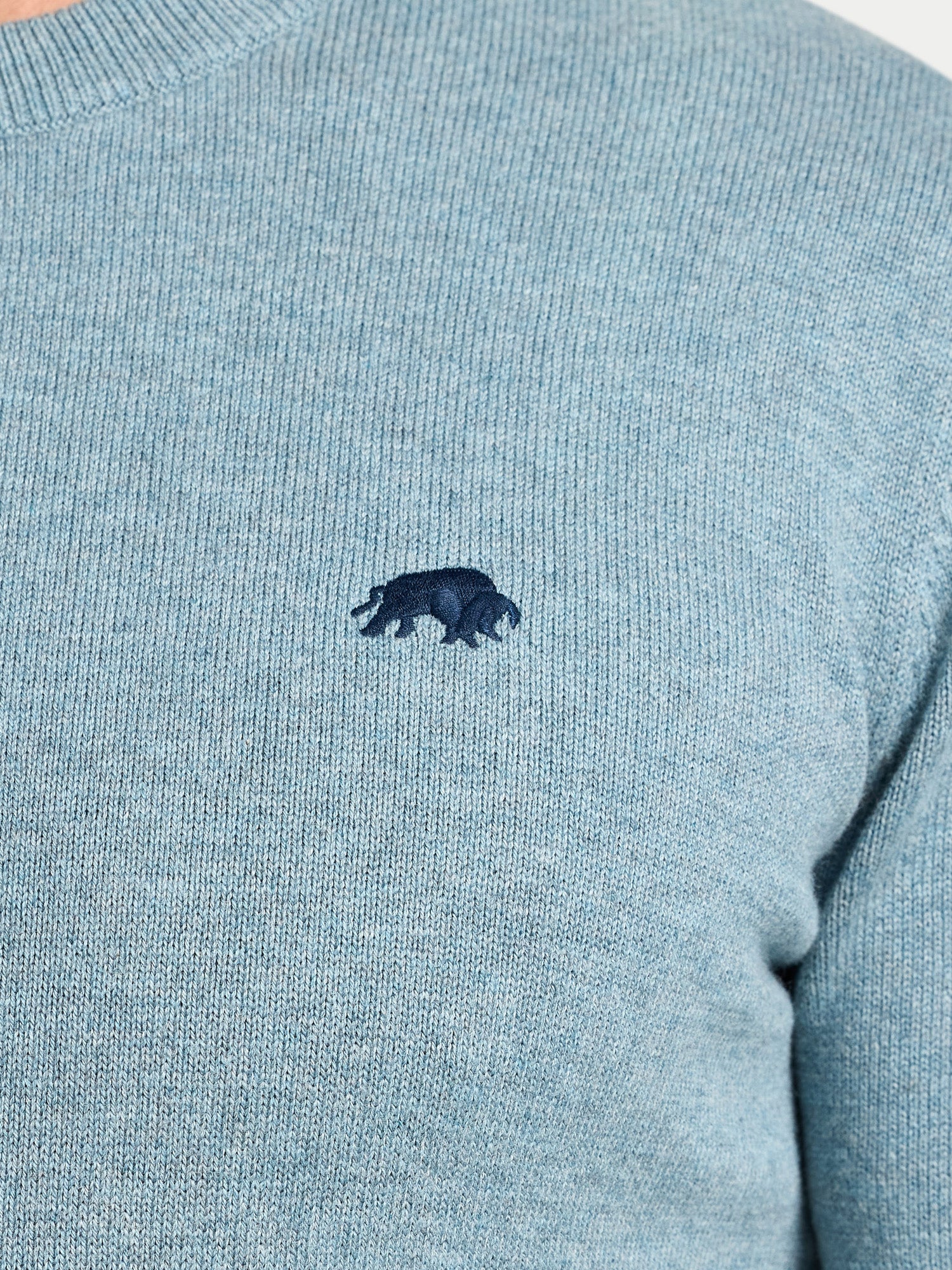 Close-up of a light blue sweater with a dark blue logo on a white background