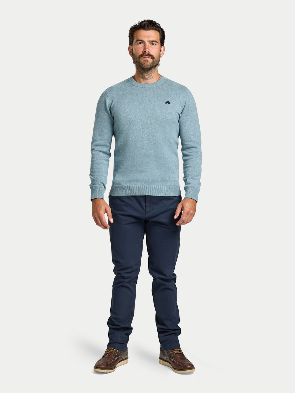 Man wearing a light blue sweater and dark pants on a white background