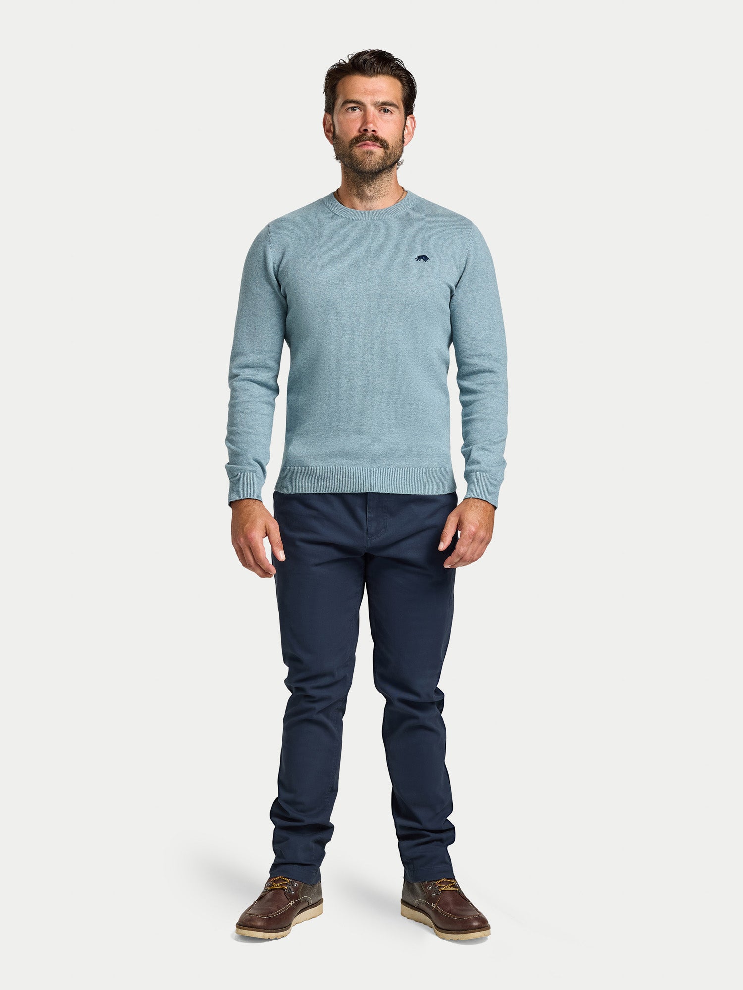 Man wearing a light blue sweater and dark pants on a white background