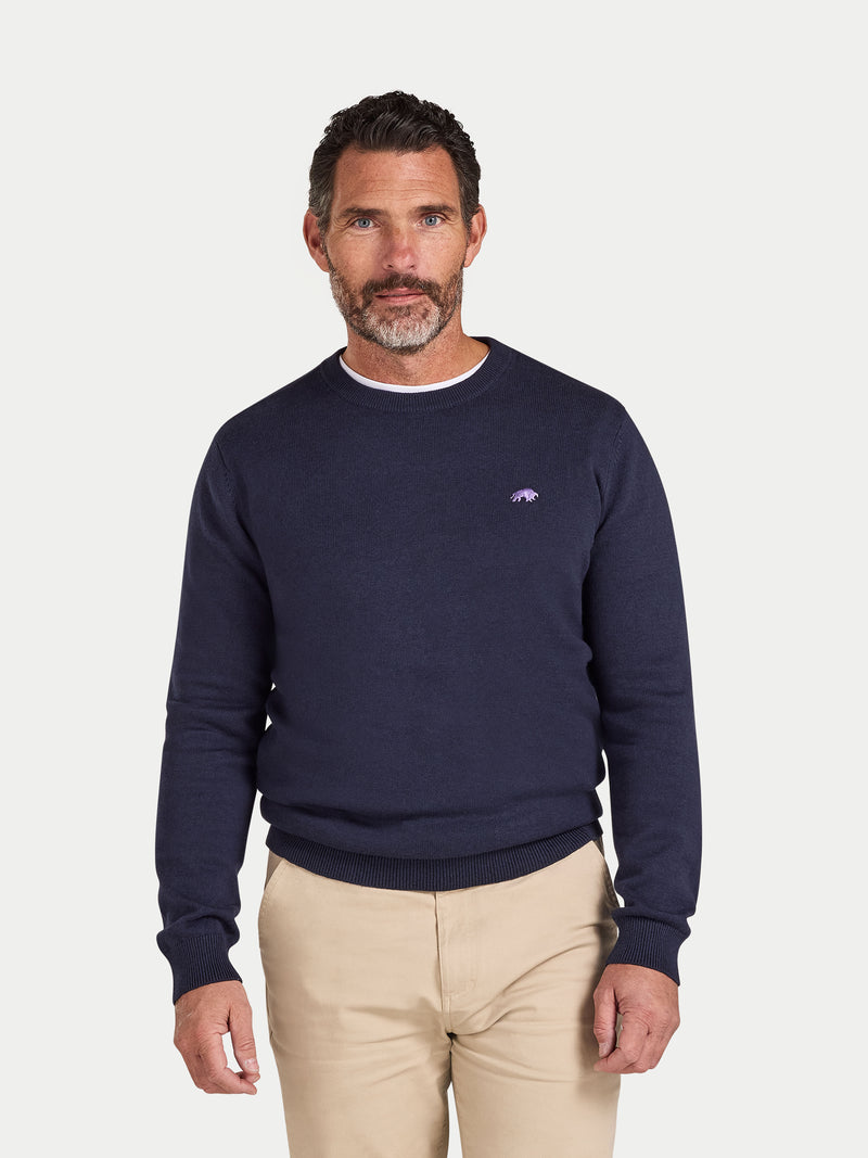 Man wearing a navy blue sweater with a logo on a white background