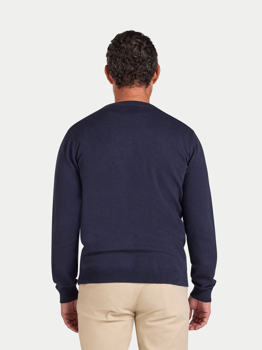 Man wearing a navy sweater and beige pants on a light gray background