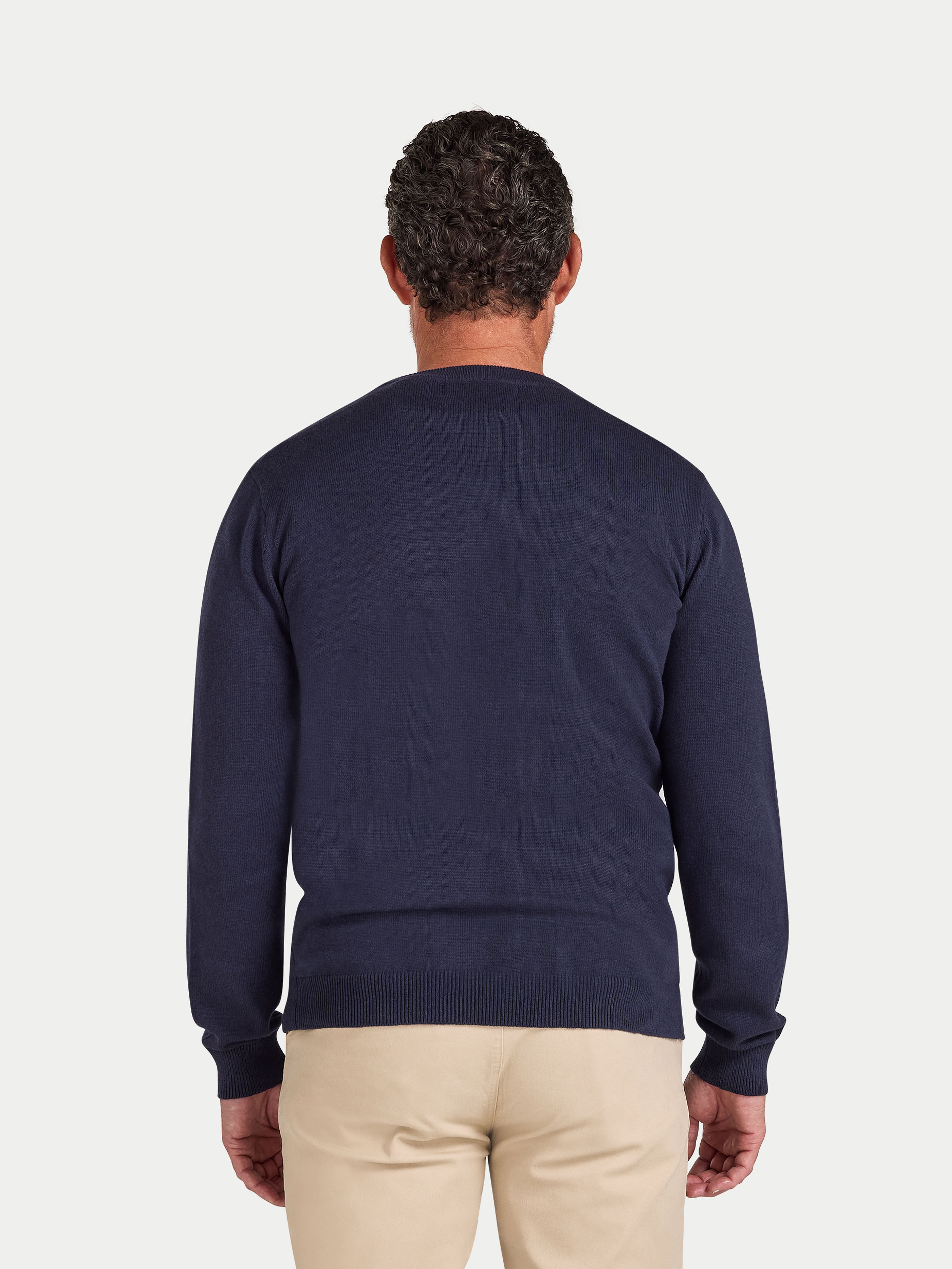 Man wearing a navy sweater and beige pants on a light gray background